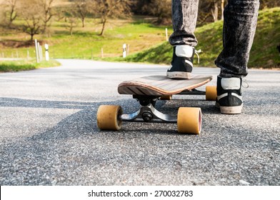 Longboard and feet of young boy in sneakers on a road