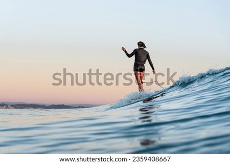 Longboard surfer riding a wave at sunrise.