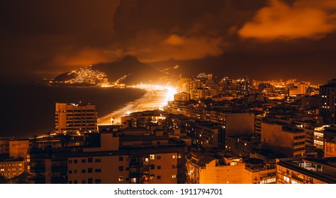 A long-exposure night cityscape in warm tones with a coastal Ipanema and Leblon districts of Rio de Janeiro, Brazil, a motion-blurred sky, highly illuminated beach, and plenty of residential houses