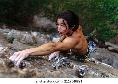 A long-haired Asian sportsman is engaged in rock climbing in the fresh air. Athlete's tanned hands smeared with magnesia powder