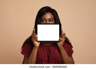 Long-haired Black Woman Hiding Her Face Behind Digital Tablet With Empty Screen, African American Lady Showing Nice Dating Mobile Application On Pad, Mockup, Beige Studio Background