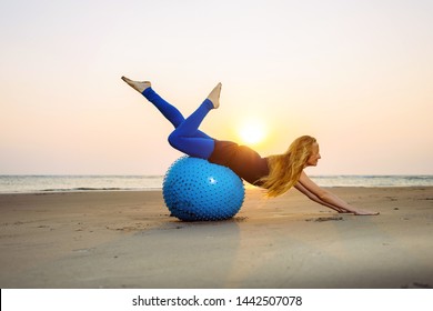 Long-haired blonde is engaged in Pilates on a training ball on the beach during sunset. Fit woman stretching her body using fitness ball. Concept of Health. - Shutterstock ID 1442507078