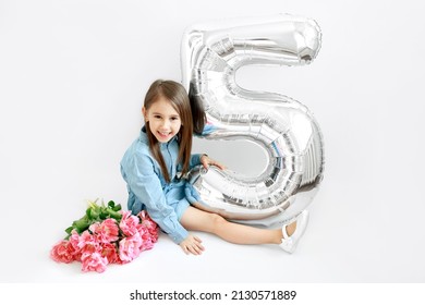 A Long-haired Brunette Girl Is Sitting With A Bouquet Of Flowers And A Large Balloon In The Shape Of The Number Five. A Cute Cute Child Is Celebrating His First Anniversary - The Fifth Anniversary.