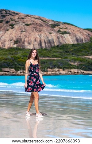 a long-haired girl in a black dress with roses walks along a paradise beach with white sand and turquoise water and orange rocks, cape le grand national park near esperance, western australia