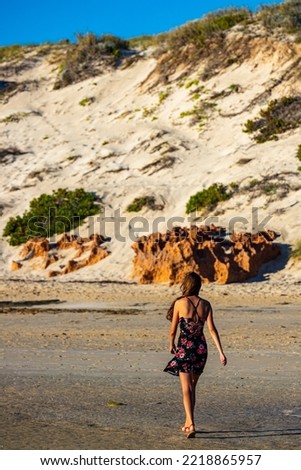 long-haired girl in black dress walks on coral bay beach at sunset; Australian beach with cliffs and coral reef; romantic walk at sunset