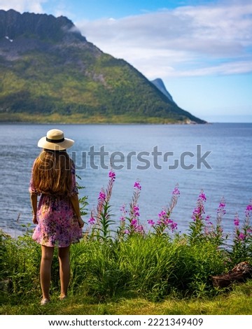 a long-haired girl in a colourful dress enjoys the sunny weather on the island of senja, norway, purple flowers and huge moss-covered mountains in the norwegian cliffs