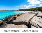 long-haired girl in dress sits on rocks enjoying the view of paradise beach with white sand and turquoise water, cape le grand national park, western australia