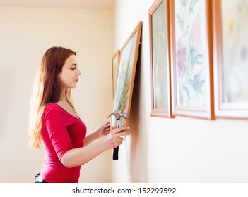 Long-haired Girl Hanging  Pictures In Frames On Wall At House