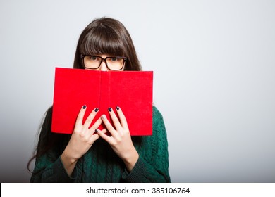 long-haired girl hides behind the book, a student in isolation on a gray background