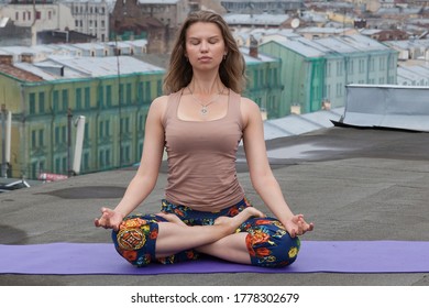 Long-haired girl meditates on the roof in bright pants