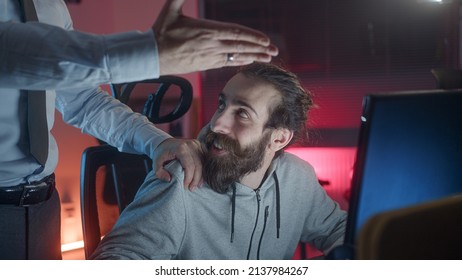 Long-haired hippie looking man playing games at the computer, employer man puts his hand on hippie looking teenager's shoulder asking what he is doing