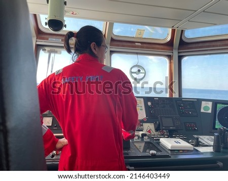 a long-haired male sailor wearing a red coverall was piloting the ship, maneuvering the ship to dock. a seafarer under controlling vessel due to maneuver for alongside at jetty