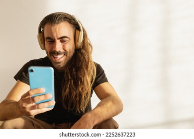 long-haired man reading a message laughing, wearing headphones - Powered by Shutterstock