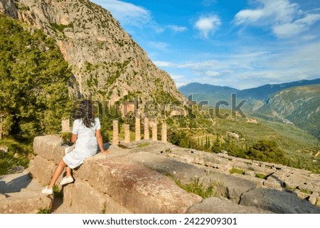 A long-haired woman from behind looking at  Apollo Temple or Apollonion and its doric pillars in sunset. Tourist spot, famous for oracle at the sanctuary dedicated to Apollo. Mount Parnassus, Delphi.