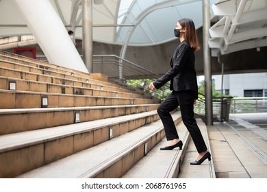 A long-haired woman wearing a mask, suit jacket, trousers and black shoes is walking up the stairs. - Powered by Shutterstock