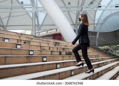 A long-haired woman wearing a mask, suit jacket, trousers and black shoes is walking up the stairs. - Powered by Shutterstock