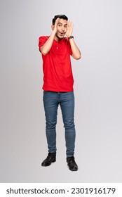 longshot of happy asian man with funny face in red T-shirt snooting sounding boh put his hands besides his face, isolated on gray background.
