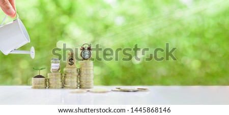 Long-tern investment, time value of money concept : Clock, US dollar bag, glass jar, a small tree on steps of rising coins. Hand pour water from a watering can, depicts asset growth from investment