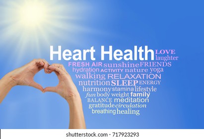 Look After and Love your Heart Word Cloud - pair of hands making a heart shape with a HEART HEALTH word cloud to the right  on a blue sky and sun burst background
