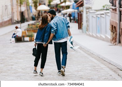 Look from behind at the couple of tourists holding their hands together while walking around the city