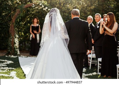 Look From Behind At Father Leading Bride In Luxuriant Wedding Dress To Altar