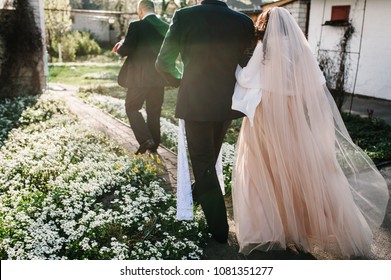 Look from behind at father leading, leads marvelous bride hidden under the veil in luxuriant wedding dress to the altar along park with groom at wedding ceremony. - Powered by Shutterstock