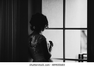 Look from behind at thoughtful bride in lace dress looking through the window - Powered by Shutterstock