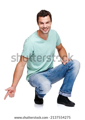 Look down here. A young man crouching and pointing towards something while isolated on a white background.