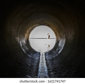 A look form a pipe looking at the beach surrounded by the sea with people in it under sunlight