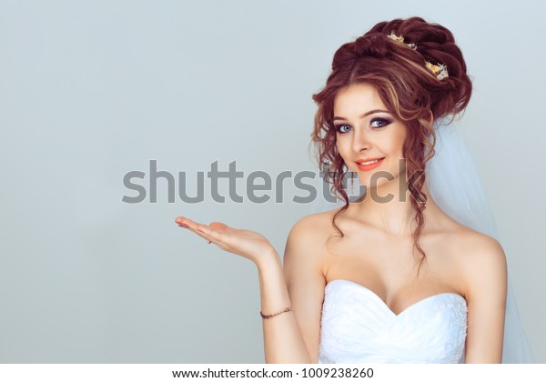 Look here, advertisement. Happy woman smiling\
showing look here at copy space at my text, product gesture with\
hand isolated light blue\
background
