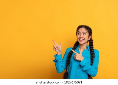 Look Here. Portrait Of Positive Happy Indian Lady Pointing Two Fingers Aside At Copy Space Advertising Your Text, Standing Isolated Over Yellow Studio Background. Smiling Woman Showing Free Place