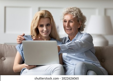 Look, mommy, it is easy. Caring grown up daughter teaching explaining retired mother how to work with laptop apps, happy old grandmother sits on couch with adult grandchild watching video on pc screen - Powered by Shutterstock