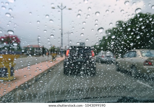 Look on wet city through windshield\
from inside the car at rain weather. Blurry background wallpaper\
traffic light with raindrop on windows in raining day. \

