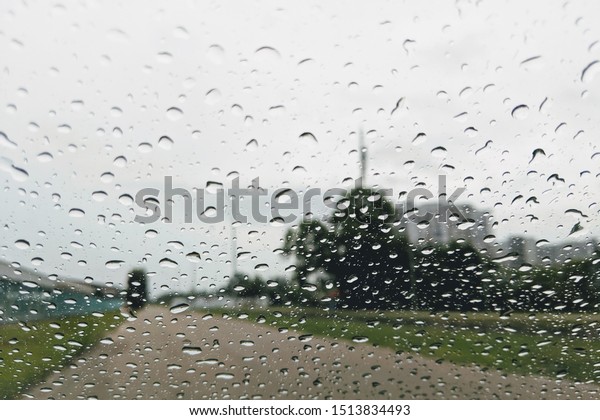 Look on wet city through windshield from inside the\
car at rain weather. Blurry background wallpaper with raindrop on\
windows in raining day.