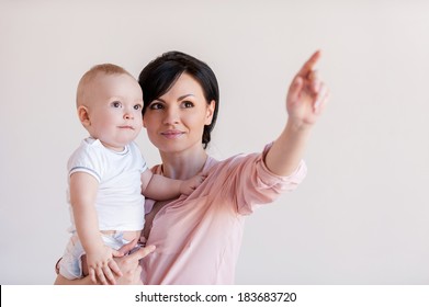 Look over there! Beautiful young mother holding baby and pointing away 