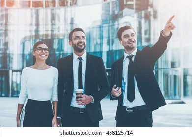 Look Over There! Three Joyful Young Business People Looking Away And Smiling While Standing Outdoors