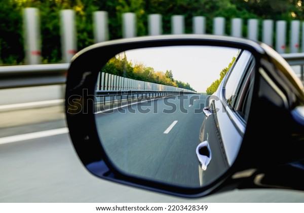 Look in the rear view mirror of a car. Car driving\
on the road.