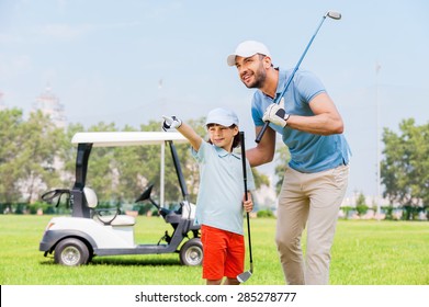 Look at that! Cheerful young man embracing his son and looking away while standing on the golf course