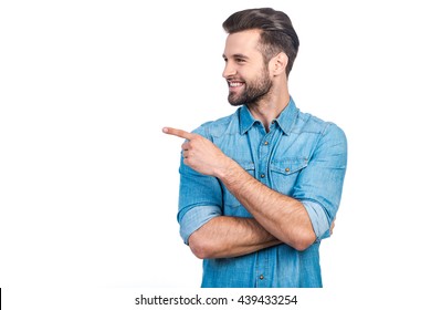 Look At That! Happy Young Handsome Man In Jeans Shirt Pointing Away And Smiling While Standing Against White Background 