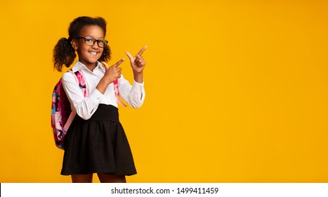 Look There. Black Elementary Student Girl Pointing Fingers At Copy Space Over Yellow Background. Panorama, Studio Shot