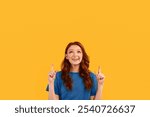 Look There. Cheerful Red-Haired Girl Pointing Fingers Up At Copy Space Posing Over Yellow Background. Studio Shot