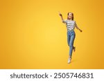 Look there. Joyful girl jumping and pointing on copy space, showing something on yellow background