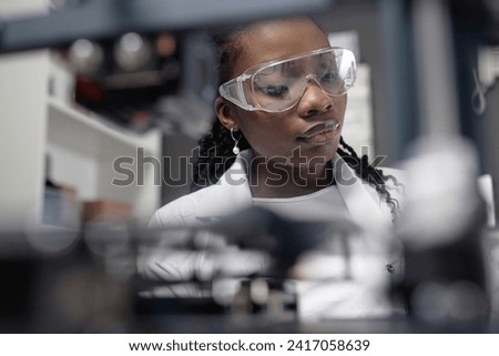 Look through blurred 3D printer components of young Black woman laboratory specialist in protective goggles