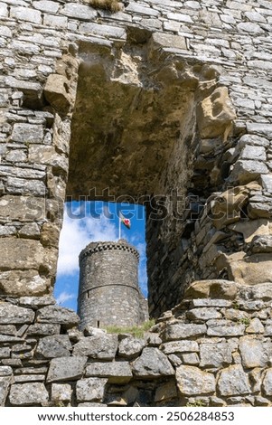 Look through large hole in outer wall of fortification Harlech Castle in Harlech, Gwynedd, Wales, UK built on rocky knoll by Edward I during invasion of Wales with flag of Wales visible on tower