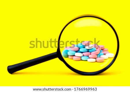 A look through a magnifying glass at a pile of multicolored pills on a yellow background. Search the ingredients of medicines. Identify fake and safe drugs in the pharmaceutical industry. Copy space.