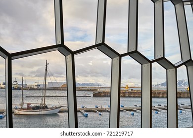 Look through patterned windows at the dockside on the background of mountains and cloudy sky in Reykjavik in Iceland. There are vessels in the harbor. Horizontal.