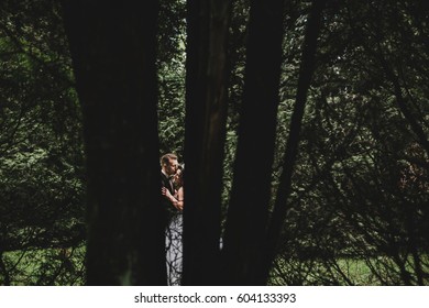 Look through thin trees at wedding couple kissing behind them