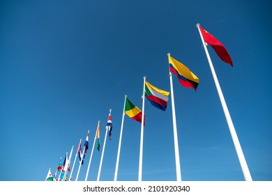 Look up view to the row of flags attached to the poles, over blue sky background, represent various countries. 