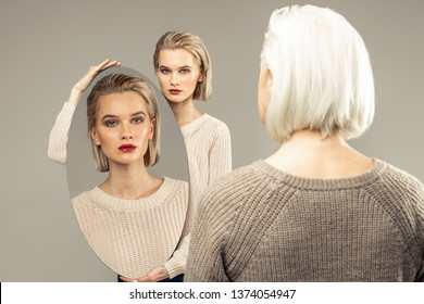 Look at you. Nice beautiful young woman holding a mirror while standing in front of herself old
