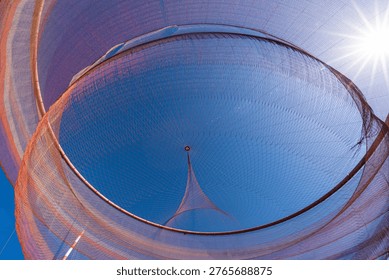 Looking up at abstract net structure forming circular pattern with sun and clear blue sky background
